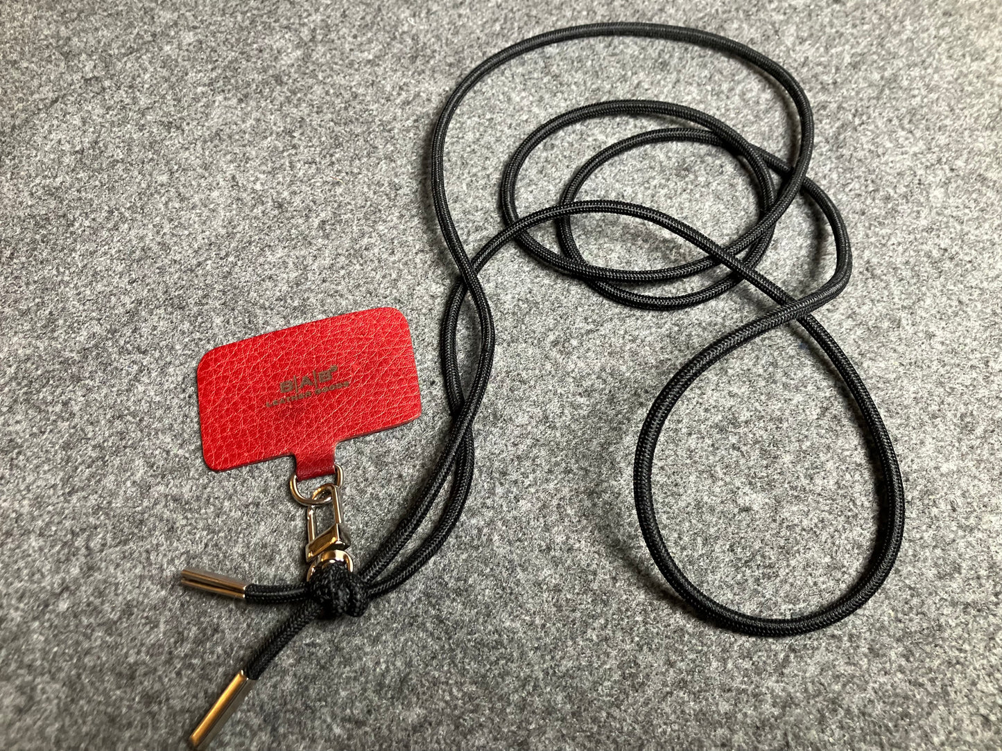 Support pour téléphone portable en Cuir Véritable Pleine Fleur tanné végétal au tanin gravé au laser & Bandoulière/Collier/Bracelet Cordon Élastique Noir, avec 1 Mousqueton et 2 Embouts argentés.- SC57