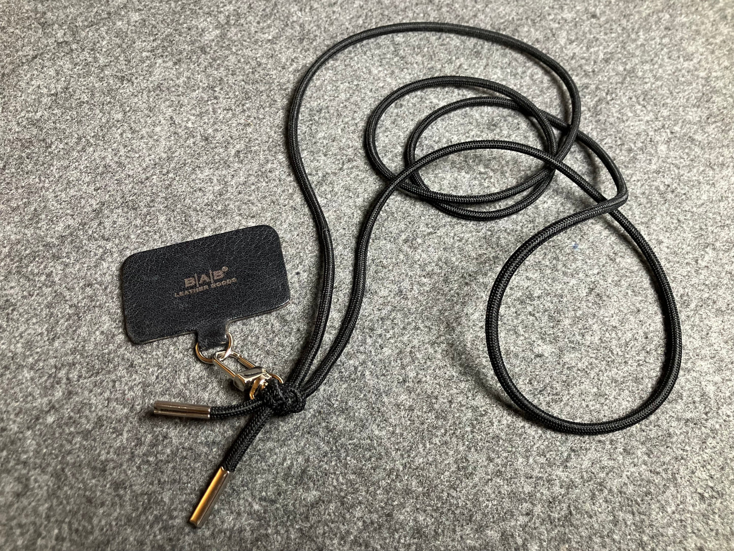 Support pour téléphone portable en Cuir Véritable Pleine Fleur tanné végétal au tanin gravé au laser & Bandoulière/Collier/Bracelet Cordon Élastique Noir, avec 1 Mousqueton et 2 Embouts argentés.- SC57