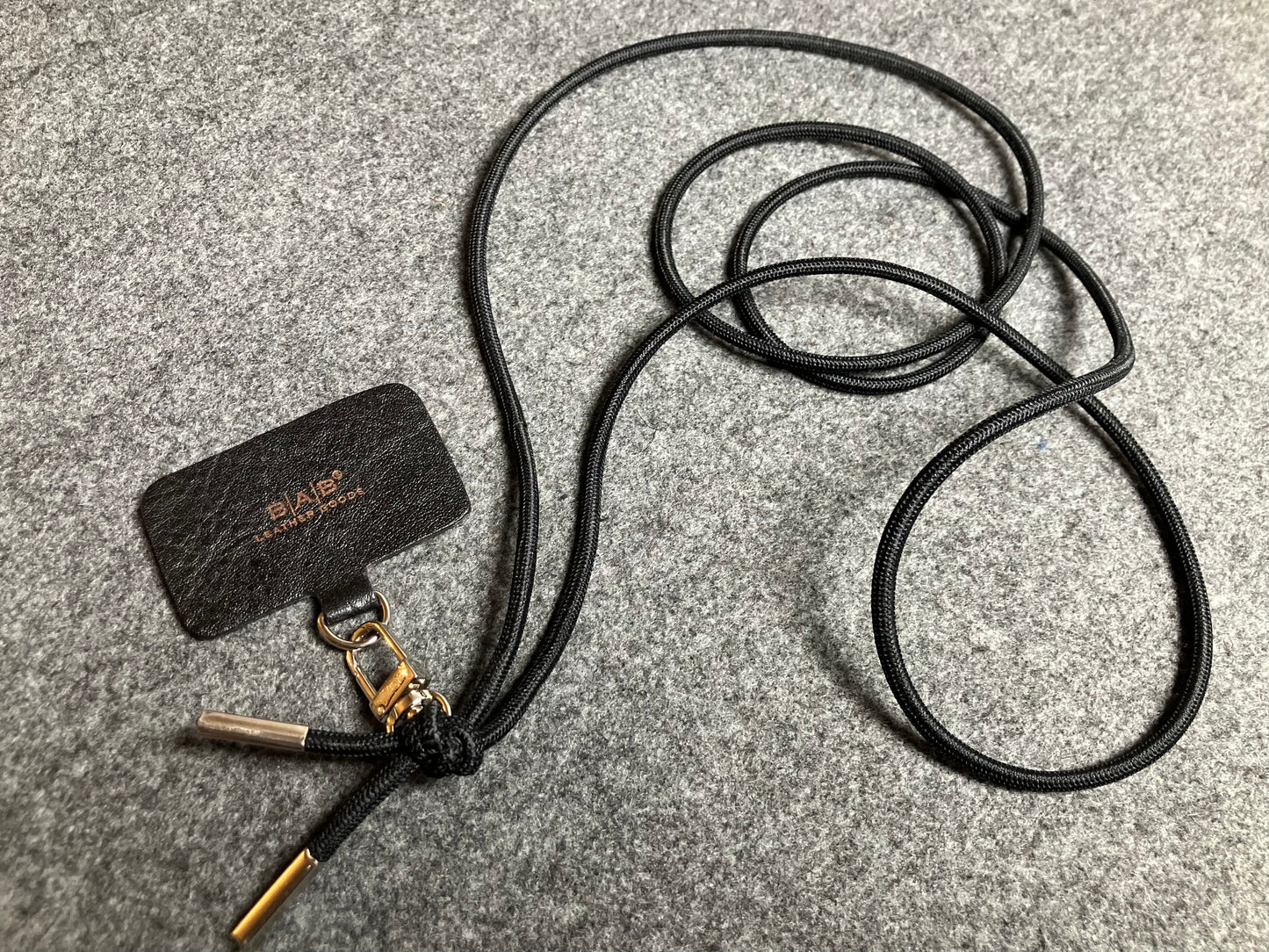 Support pour téléphone portable en Cuir Véritable Pleine Fleur tanné végétal au tanin gravé au laser & Bandoulière/Collier/Bracelet Cordon Élastique Noir, avec 1 Mousqueton et 2 Embouts argentés.- SC57