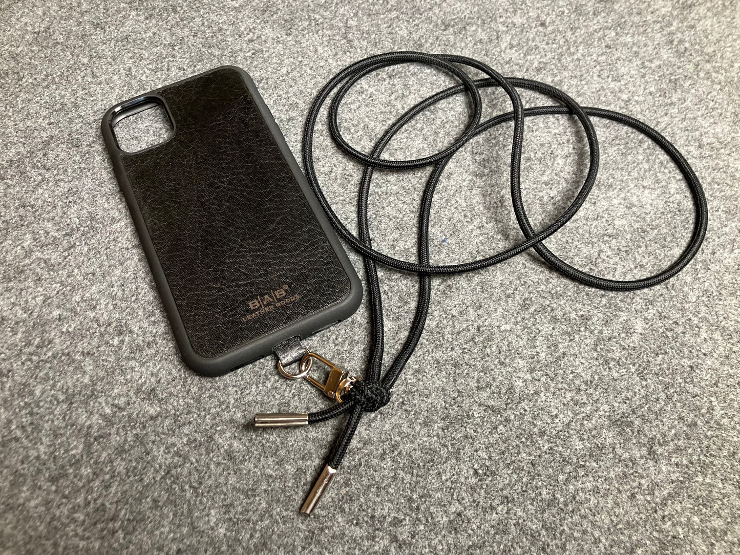 Support pour téléphone portable en Cuir Véritable Pleine Fleur tanné végétal au tanin gravé au laser & Bandoulière/Collier/Bracelet Cordon Élastique Noir, avec 1 Mousqueton et 2 Embouts argentés.- SC57