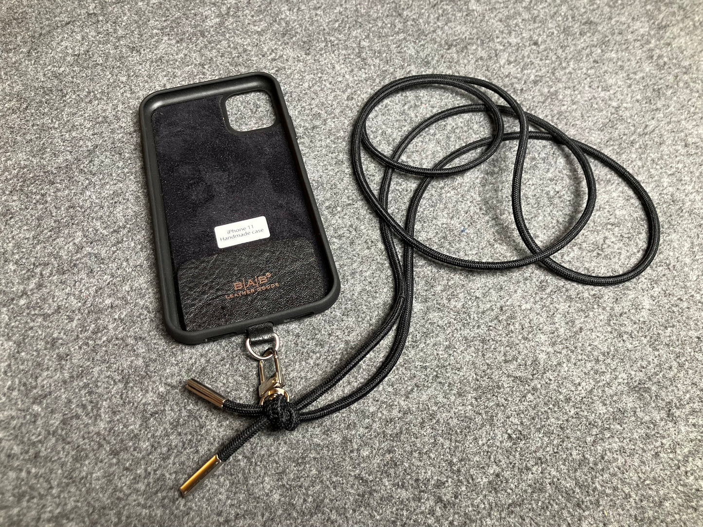Support pour téléphone portable en Cuir Véritable Pleine Fleur tanné végétal au tanin gravé au laser & Bandoulière/Collier/Bracelet Cordon Élastique Noir, avec 1 Mousqueton et 2 Embouts argentés.- SC57