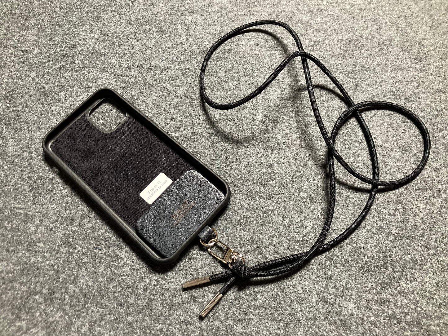 Support pour téléphone portable en Cuir Véritable Pleine Fleur tanné végétal au tanin gravé au laser & Bandoulière/Collier/Bracelet Cordon Élastique Noir, avec 1 Mousqueton et 2 Embouts argentés.- SC57
